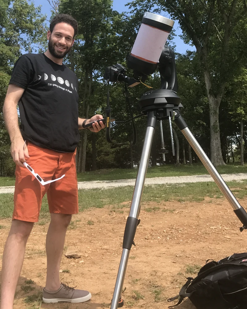 Ben Koevary beside a telescope on a tripod, in a field in Innsbrook, Missouri.