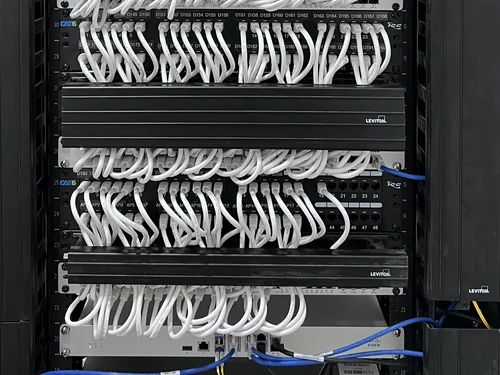 A network rack: stacked patch panels with every port labelled, patched in white cable down to Cisco switches, inside vertical cable management.