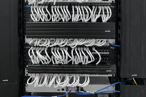 A network rack: stacked patch panels with every port labelled, patched in white cable down to Cisco switches, inside vertical cable management.